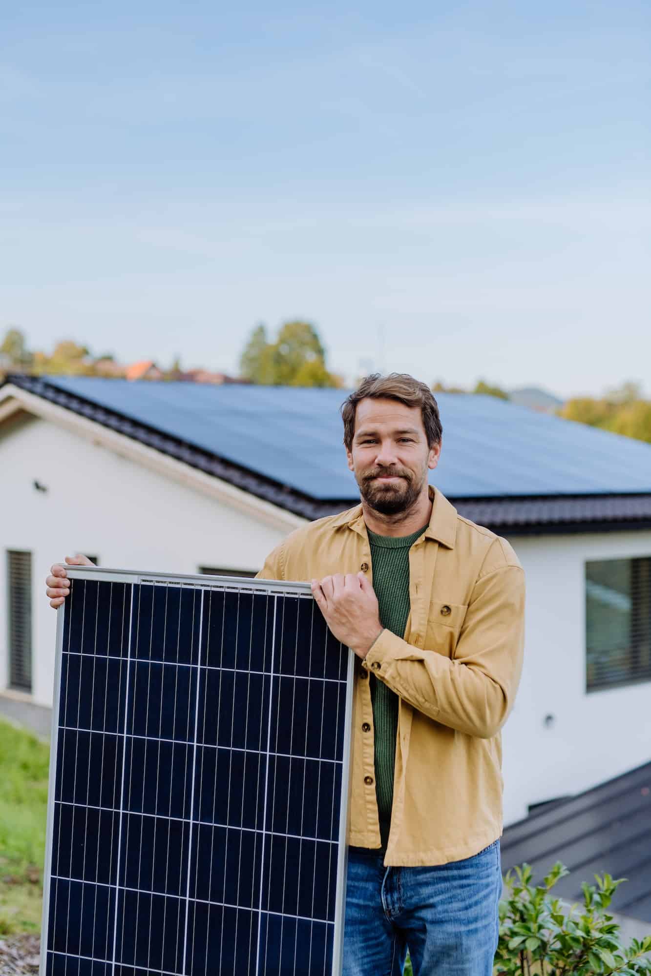Mature man holding solar panel near his house with solar panels on the roof. Alternative energy